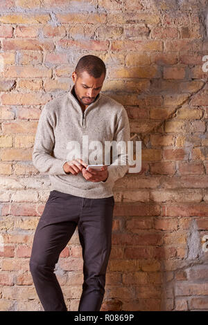 Eine ernsthafte gutaussehenden jungen Mann mit seinem Smartphone in einem Pullover. Stockfoto