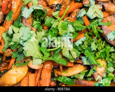 Frisch gehackten Koriander auf gebratene Stücke von Hühnerfleisch mit Gemüse ganz nah beim Kochen ein szechuan Hühnchenspeise Stockfoto