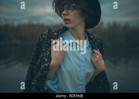 Porträt der jungen Frau in hat neben dem See auf dem Hintergrund der Himmel am Abend in der Dämmerung während. Stockfoto