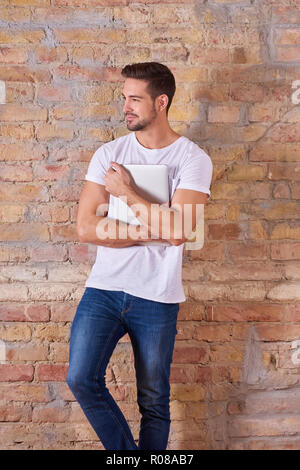 Eine selbstbewusste hübscher junger Mann mit einem Notebook-PC in einem weißen T-Shirt. Stockfoto
