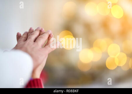 Ein junges Paar, das Hände an Weihnachten mit Licht im Hintergrund. Stockfoto