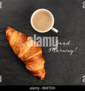 Guten Morgen Karte. Ein Foto von einem Croissant mit einer Tasse Kaffee, geschossen von oben auf einem schwarzen Hintergrund mit einem Platz für Logo Stockfoto