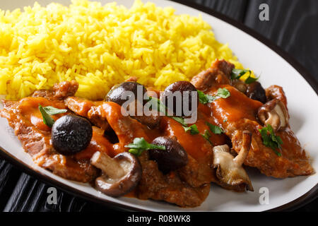 Rindfleisch fricando Eintopf mit Soße und Pilze mit Beilage von gelben würzigen Reis close-up auf einem Schild auf einem Schwarzen Tisch. Horizontale Stockfoto