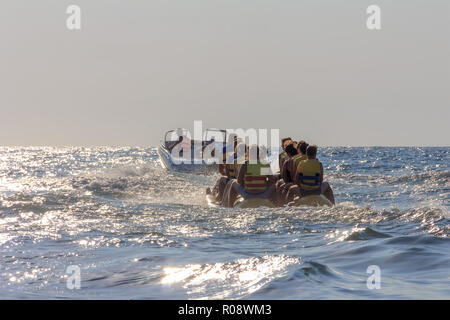 Glückliche urlauber Touristen fahren eine aufblasbare Banane im Meer Stockfoto