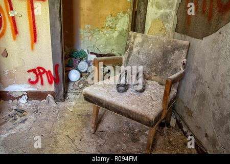 Ein verlassenes Paar Schuhe sitzen auf einem dreckigen Stuhl in einem verlassenen Gebäude in Detroit. Stockfoto