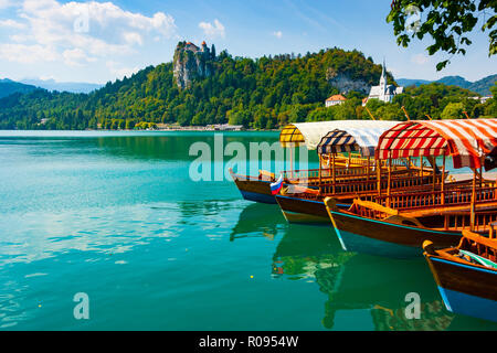 Traditionelle pletna Boote auf dem Wasser des Sees Bled mit Burg von Bled Klippe auf dem Hintergrund, Obere Krain, Slowenien Stockfoto