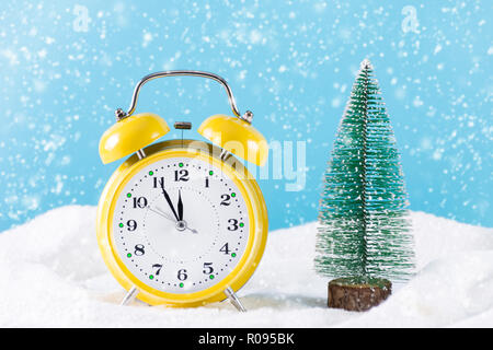 Retro Wecker und Weihnachten Tannenbaum auf Schnee und es schneit im Winter Tag. Uhr ist in der Farbe Gelb und Schneeflocken fallen. Weihnachten und neues Jahr Stockfoto