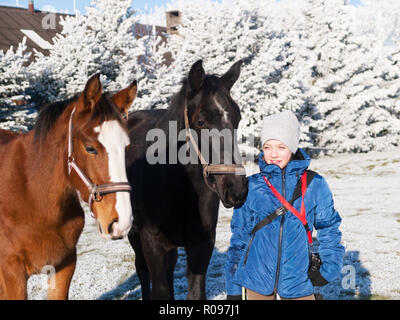 Junge Mädchen und zwei Fohlen von Sport Pferde auf der Weide im Winter Stockfoto