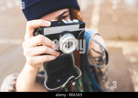 Junges Mädchen mit Tattoos und Dreadlocks in einem blauen Hut Fotografien eine vintage Kamera auf dem Hintergrund einer Betonwand Stockfoto