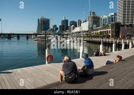 Menschen ruht auf einem Spaziergang im Sonnenschein, mit dem Kai, Boote und Gebäude des Darling Harbour. Stockfoto