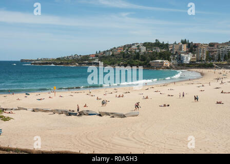 Blick entlang der Bucht von Coogee Beach, Sydney mit goldenem Sand, türkisfarbenes Meer und in der Ferne Menschen Sonnenbaden und Schwimmen. Stockfoto