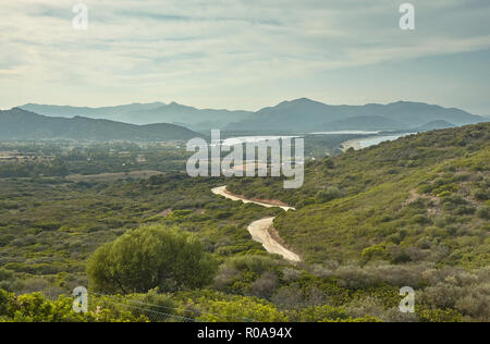 Die hügelige Landschaft, die typisch für die Küste im Süden von Sardinien mit einer Schmutz Weg flussabwärts Richtung Meer. Stockfoto