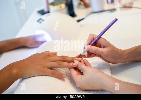 Close-up Kosmetikerin Malerei Nägel eine Frau mit einem Pinsel in ein Nagelstudio. Kunden erhalten eine Maniküre. Stockfoto