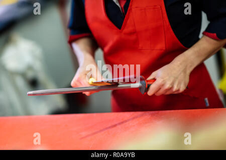 Junge weibliche Metzger Schärfen eines Messers in einer Metzgerei Stockfoto