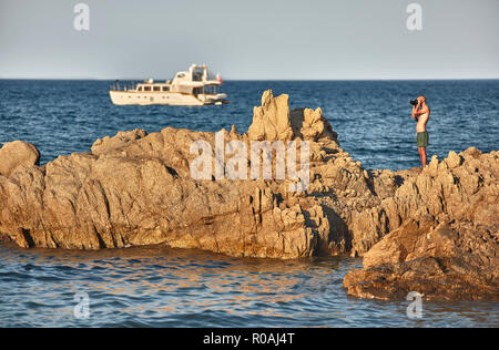 Fotograf Absicht auf das Fotografieren einer natürlichen Landschaft auf einem Felsen in der Mitte des blauen Meer bei Sonnenuntergang. Stockfoto