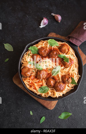Spaghetti Nudeln mit Hackfleischbällchen, Tomatensauce und frischem Basilikum in gusseisernen Pfanne. Gesunde hausgemachten italienischen Teigwaren auf rustikalen schwarzer Hintergrund mit Kopie spa Stockfoto