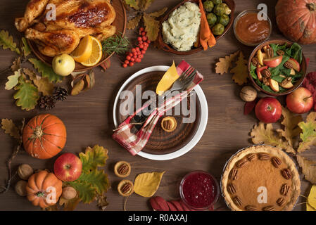 Thanksgiving Dinner Hintergrund mit der Türkei und alle Seiten Gerichte, Pumpkin Pie, Herbstlaub und saisonale Dekoration rund um die Platte, Ansicht von oben. Stockfoto