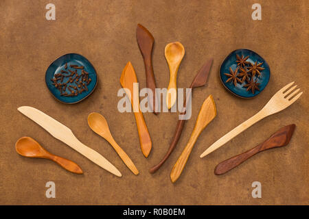 Handgefertigten Holz- Utensilien und Gewürzen auf braunem Hintergrund. Gabel, Löffel und Messer. Gewürznelken und Anis. Stockfoto