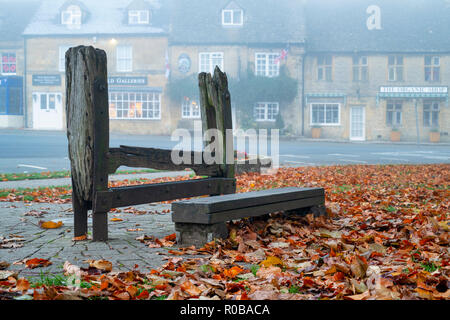 Das Dorf strafrechtlichen Stocks auf der Grünen am frühen Morgen herbst Nebel, Stow auf der Wold, Gloucestershire, Cotswolds, England Stockfoto