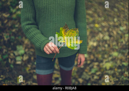 Eine junge Frau steht in den Wäldern halten ein Blatt im Herbst Stockfoto