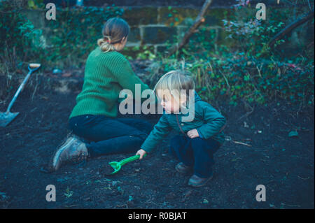 Eine Mutter und Kleinkind graben Löcher in den Garten im Herbst Stockfoto