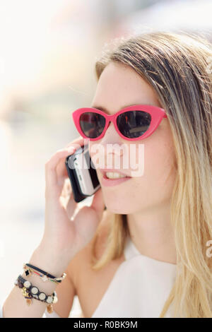 Eine junge holländische (Kaukasisch) Frau mit ihrem Mobiltelefon in der Straße an einem sonnigen Tag Stockfoto