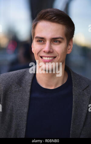 Trendige schöne glückliche Menschen bleiben auf der Straße in grauen Mantel und blauen Pullover. Stockfoto