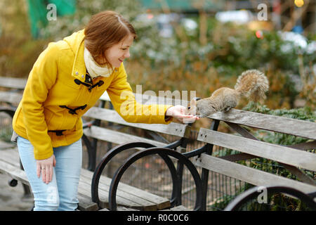 Glückliche junge Frau touristische Fütterung ein Eichhörnchen im Madison Square Park, New York City, am sonnigen Frühlingstag. Weibliche Reisende mit Blick auf die Innenstadt von Ma Stockfoto
