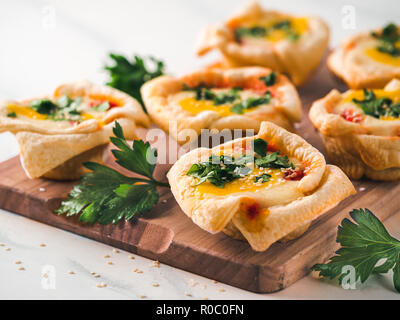 Ideen und Rezepte für eine gesunde Vegane Shakshouka Cups mit vegan Tofu, Eier und Eigelb, Gelbwurz auf weißem Marmortisch. Blätterteig Blätterteig, Tomaten und Gemüse Sauce, frische grüne Petersilie. Kopieren Sie Platz für Text Stockfoto