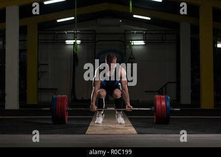 Athlet Steht auf seinem Knie und in der Nähe der Bar in der Turnhalle und bereitet das Kreuzheben zu machen Stockfoto