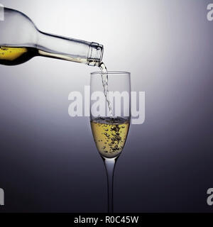 Weißwein wird aus einer Flasche in ein Glas gegossen. Beleuchtung zieht die Aufmerksamkeit auf die Glas- und gießen Wein. Stockfoto