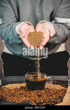 Kaffeebohnen und Instant Kaffee gießt gerade nach unten aus der Hand in eine Tasse frisch gebrühten Kaffee Stockfoto