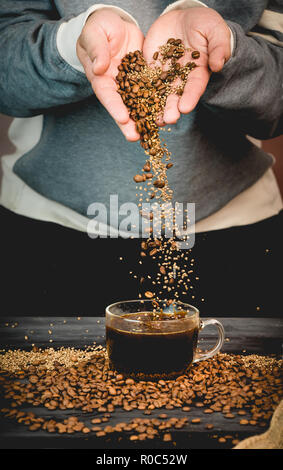 Kaffeebohnen und Instant Kaffee gießt gerade nach unten aus der Hand in eine Tasse frisch gebrühten Kaffee Stockfoto