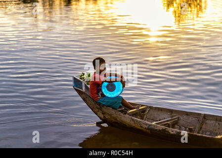 Tonle Sap, Kambodscha - Januar 04, 2017: Ein kleiner Junge auf einem Kanu trägt eine kann Wasser in den Tonle Sap See bei Sonnenuntergang Stockfoto