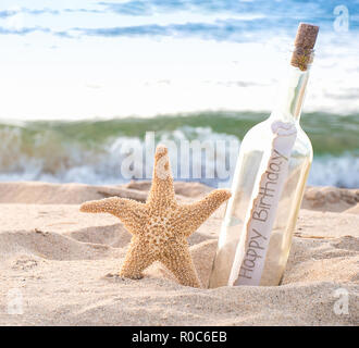 Nahaufnahme der Seesterne und happy birthday Nachricht in einer Flasche am Meer mit Wasser Hintergrund Stockfoto