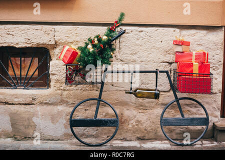 Kreative Fahrrad mit Weihnachtsbaum, Rot präsentiert, Wein Flasche in europäischen Stadt Straße. Stilvolle weihnachten Straße Dekor, festliche Dekorationen und illumi Stockfoto