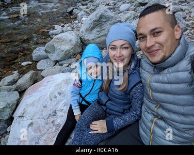 Touristen Rest nach der Wanderung und selfie am Telefon. Fotos vom Handy während der Wanderung. Familie reist. Menschen Umwelt durch Berge, Flüsse, Ströme. Mann und Frau haben wandern Rucksäcke. Stockfoto