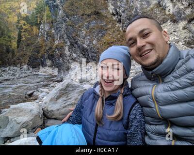 Touristen Rest nach der Wanderung und selfie am Telefon. Fotos vom Handy während der Wanderung. Familie reist. Menschen Umwelt durch Berge, Flüsse, Ströme. Mann und Frau haben wandern Rucksäcke. Stockfoto