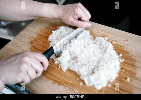 Die Hände einer Frau, die Zwiebel hacken in kleine Scheiben auf einer hölzernen Schneidebrett Stockfoto