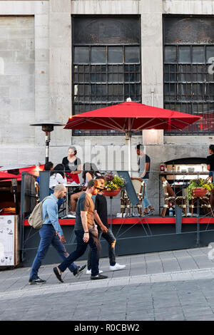 Die Menschen gehen auf die Straße und sitzen in einem Café im Freien im Alten Hafen von Montreal, Quebec, Kanada. Redaktionelle Verwendung. Stockfoto