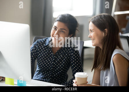 Lächelnd diverse weibliche Studierende Praktikanten im Büro in der Kaffeepause sitzen vor dem Computer, glücklich, fröhlich multirassischen Mitarbeiter chatten Stockfoto