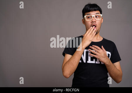 Jungen Asiatischen nerd Mann mit Brille gegen grauer Hintergrund Stockfoto