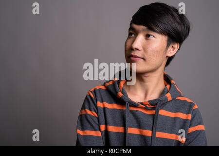 Jungen asiatischen Mann, der gestreifte Hoodie gegen grauer Hintergrund Stockfoto
