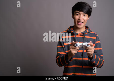 Jungen asiatischen Mann spielt Spiele gegen grauer Hintergrund Stockfoto