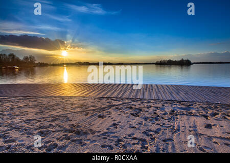 Holz- Freizeit Schwimmen deck und Sandstrand am See während der spektakulären Sonnenuntergang über dem Wasser Stockfoto