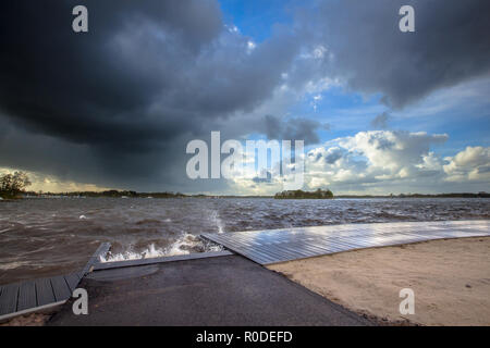 Dunkle Wolken, rauer Wind und mäßig hohe Wellen brechen auf einem Bootssteg, wenn ein Sturm kommt in über eine Holländische See Stockfoto