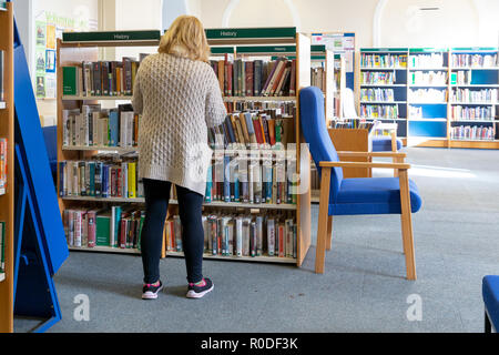 Reife, blonde Dame suchen durch die Bücher in der Geschichte der Bibliothek in Warrington, Cheshire, England, Großbritannien Stockfoto