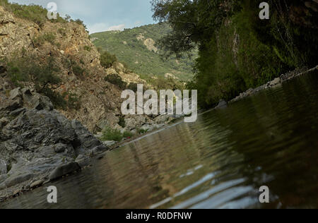 Felswand mit Vegetation bedeckt ist, die Grenze der Wasserlauf in den Bergen mit verschiedenen Felsen, die aus dem Wasser steigen: Die Ansicht von Sa Stid Stockfoto