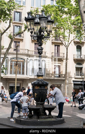 Menschen füllen Plastikflaschen mit frischem Trinkwasser aus einem alten Brunnen in Barcelona, Spanien Stockfoto