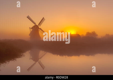 Charakteristische historische Windmühle entlang eines breiten Kanal in einem Polder Feuchtgebiet an einem nebligen Septembermorgen in den Niederlanden Stockfoto